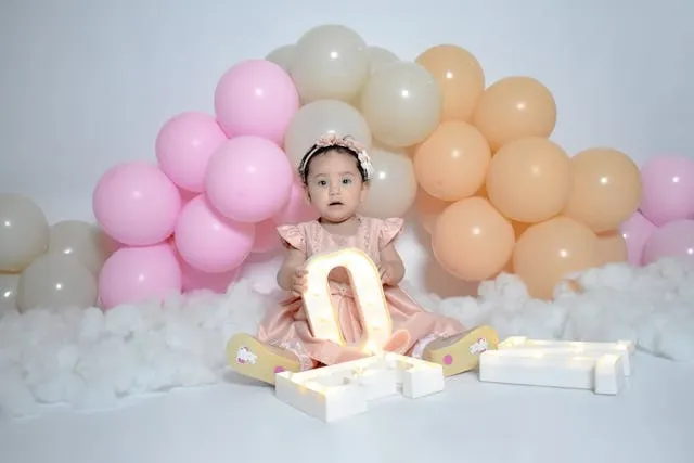 a baby sitting under a balloon arch for birthday backdrop ideas